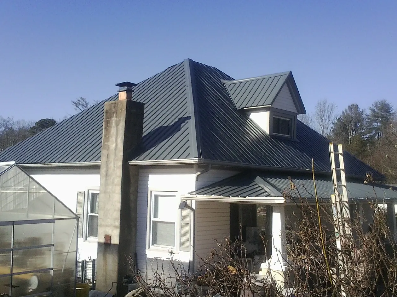 Dark blue standing seam metal roof on a white farmhouse with dormer — Slate & Tile Roof Repair by Roofing Brothers in Grover