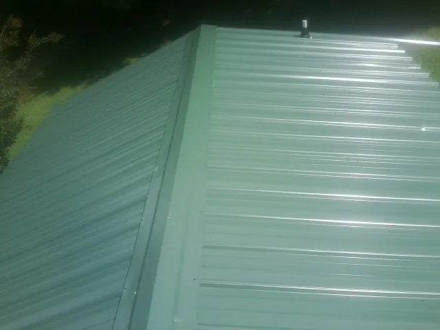New green metal panels meeting at the ridge of a roof — Flat Roof Repair work by our crew in Grover