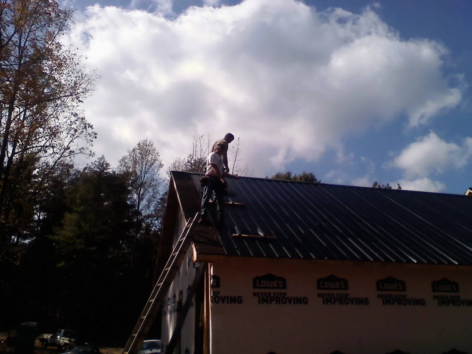 Roofer fastening dark metal panels high against a cloudy sky, from a Roof Inspection job in Grover