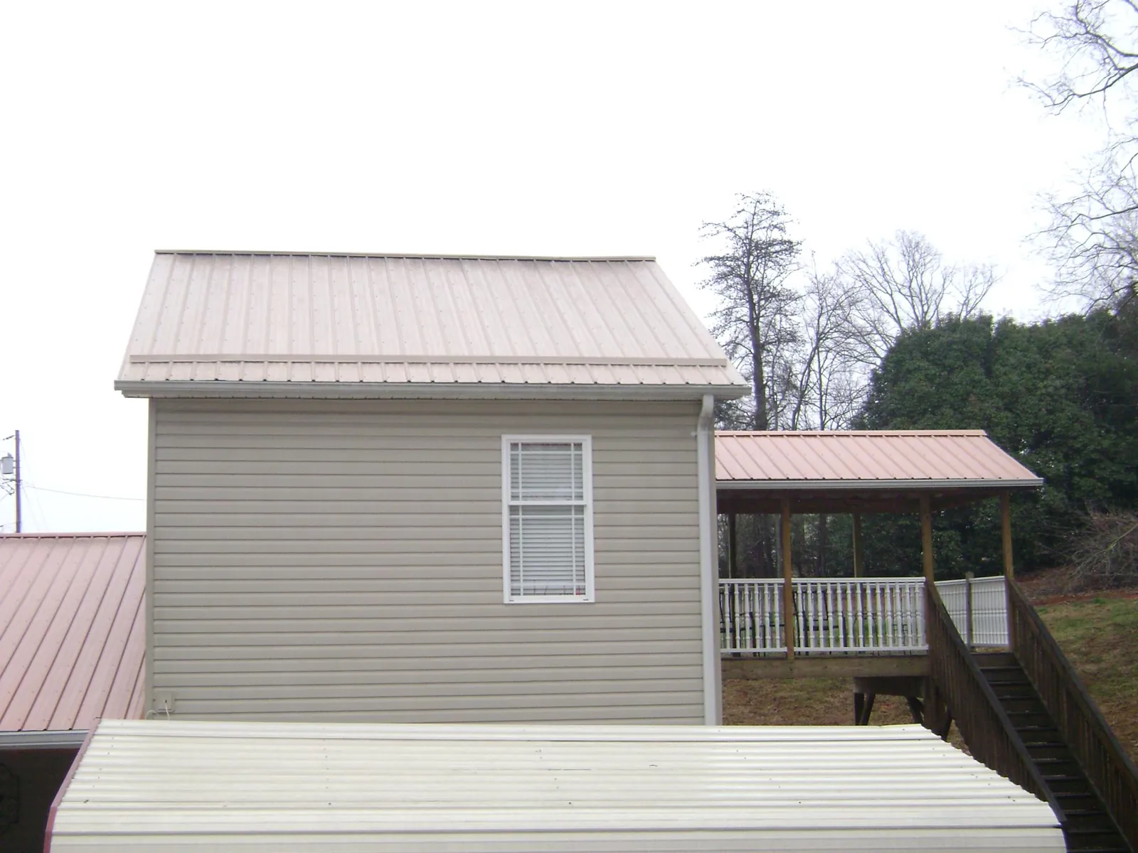 Tan metal roofs on a two story addition and attached porch, from a Roof Replacement job in Grover